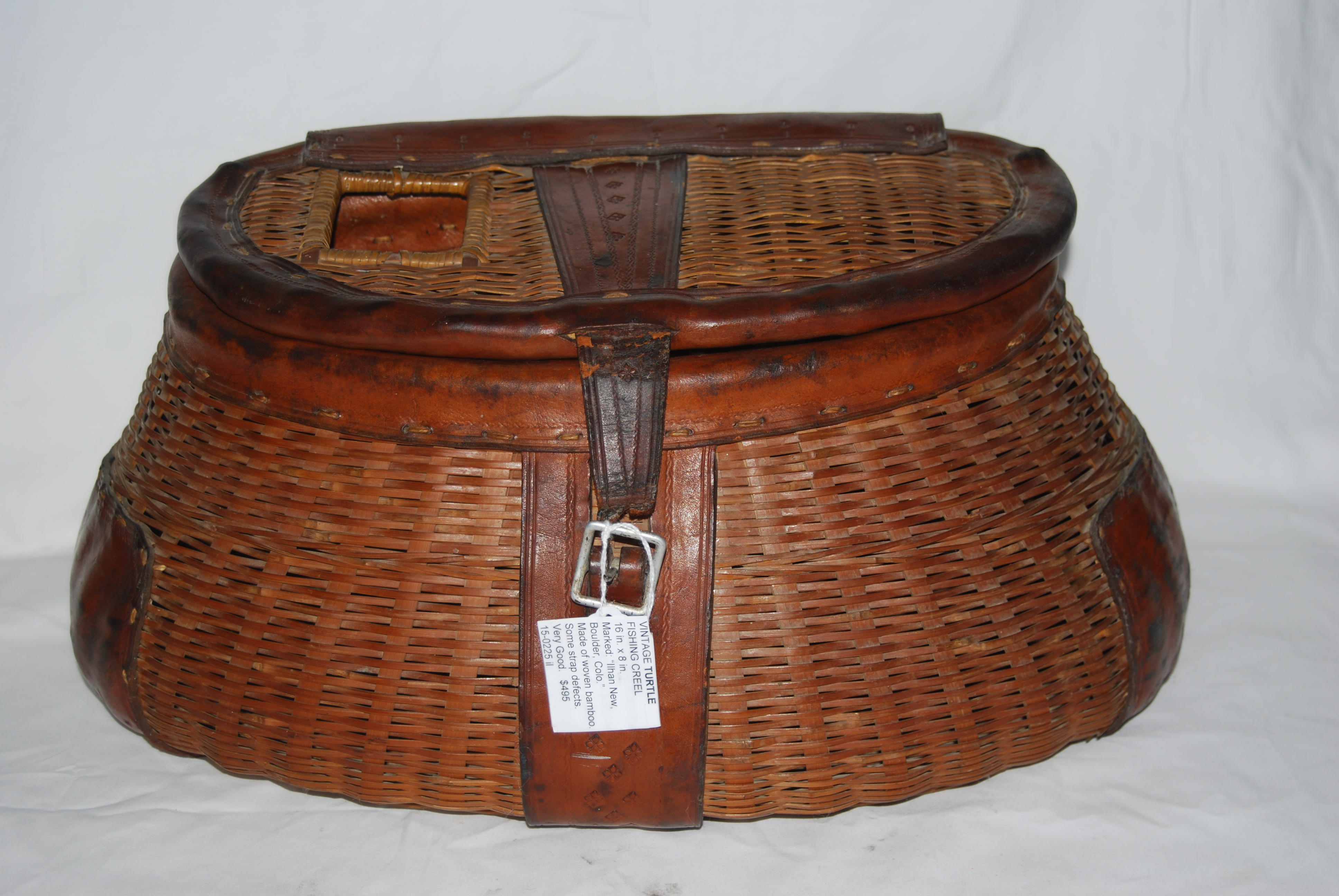 VINTAGE ANTIQUE “TURTLE” LEATHERED FISHING CREEL. Woven of split bamboo. 16  in. long X 8 in. high. Side Hole, Trimmed in Leather. Marked on base  leather strap: ”Ilhan New Boulder Colo.” SOLD