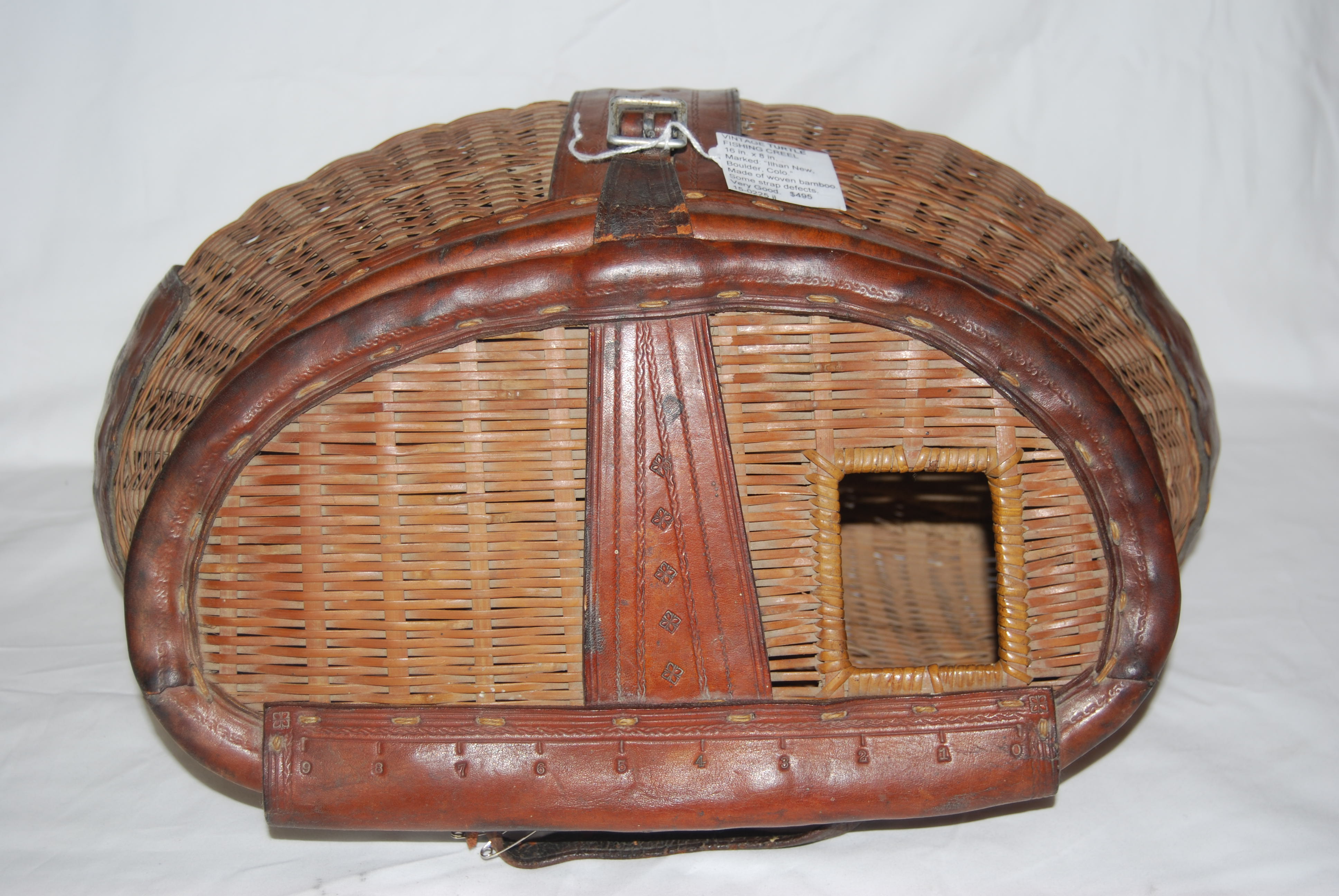 VINTAGE ANTIQUE “TURTLE” LEATHERED FISHING CREEL. Woven of split bamboo. 16  in. long X 8 in. high. Side Hole, Trimmed in Leather. Marked on base  leather strap: ”Ilhan New Boulder Colo.” SOLD